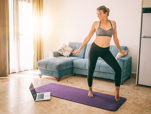 a woman taking part in a dance fitness routine in her living room with a laptop on a yoga matt